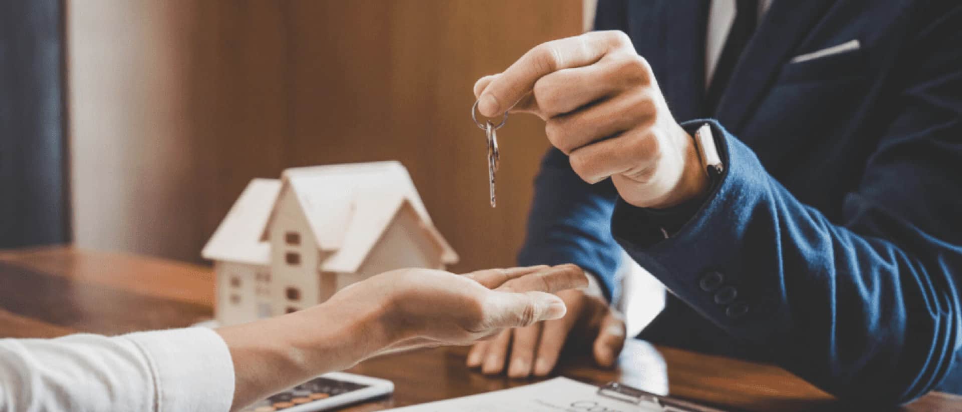 Person handing keys with a small house model