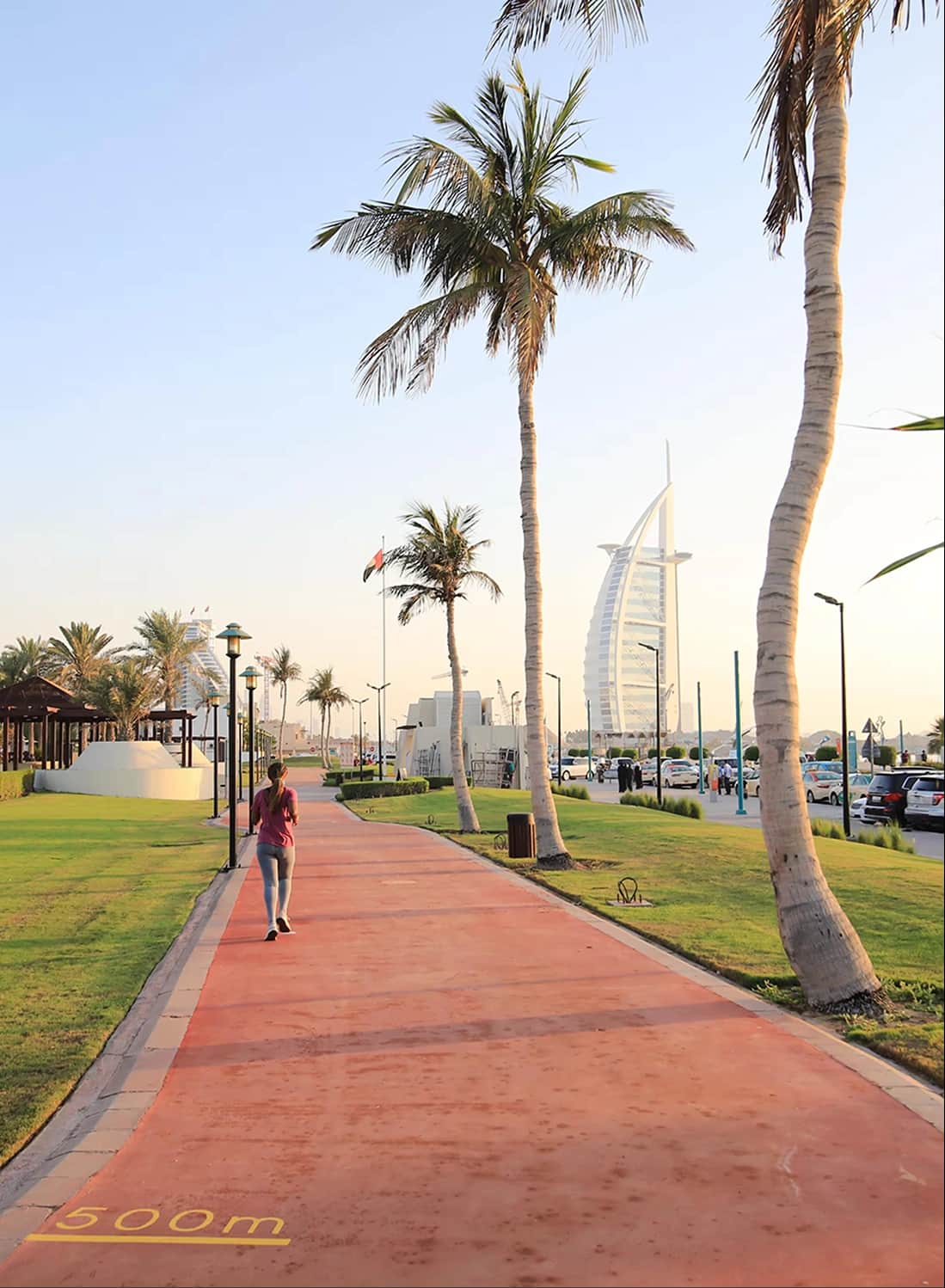 Man walking along a scenic path with palm trees and Burj Al Arab