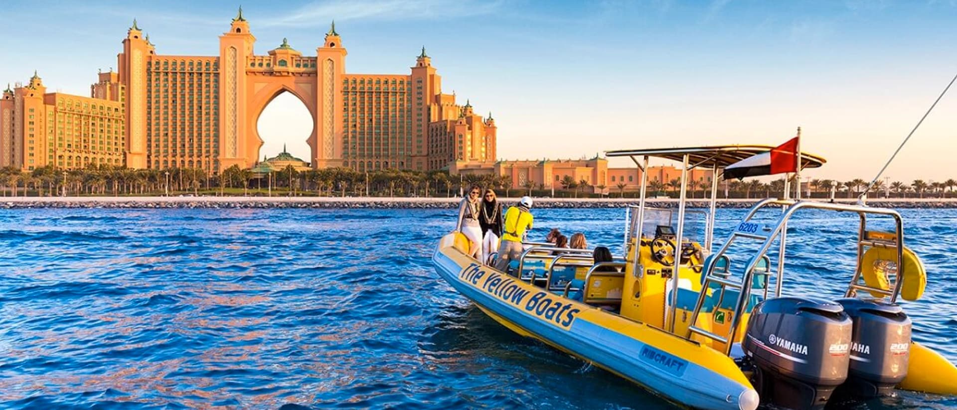 A yellow boat with tourists on board cruises in front of the Atlantis resort in Dubai