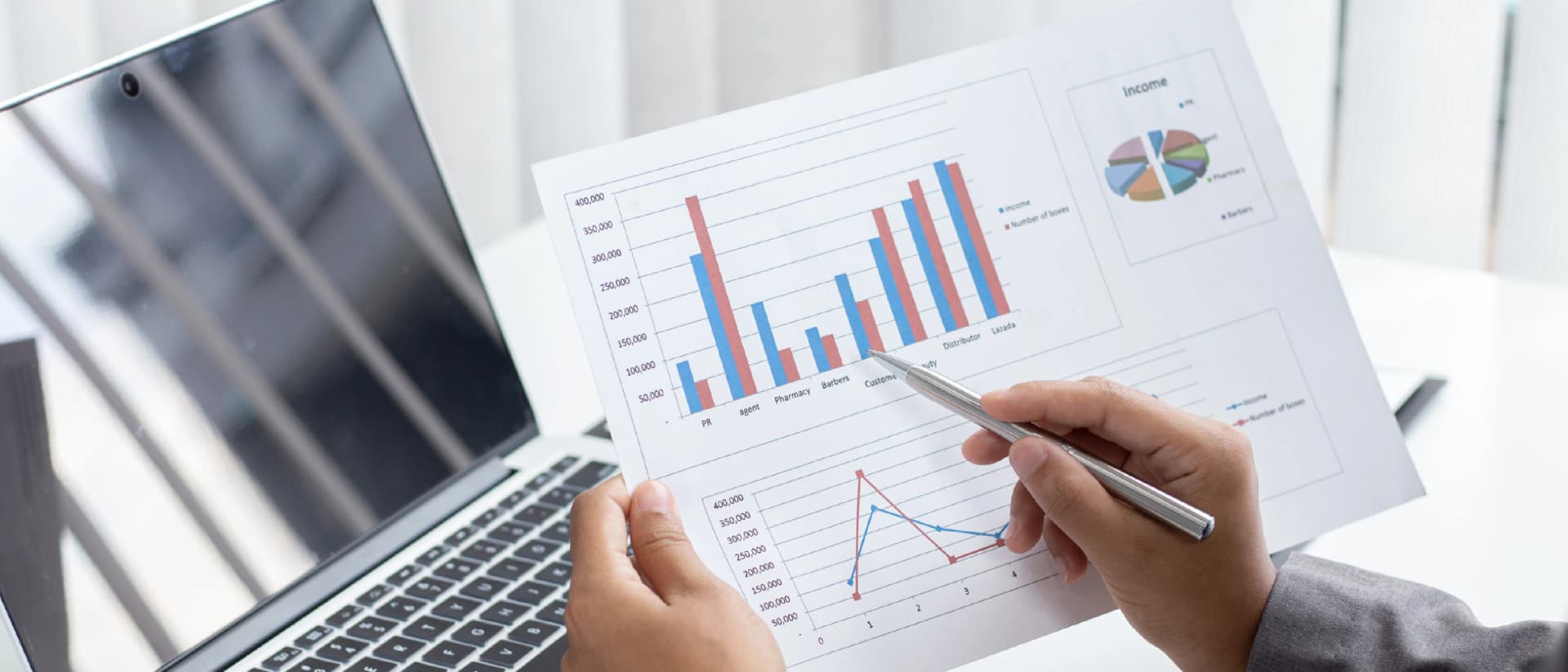 A person reviews financial documents with charts and graphs, with a laptop nearby