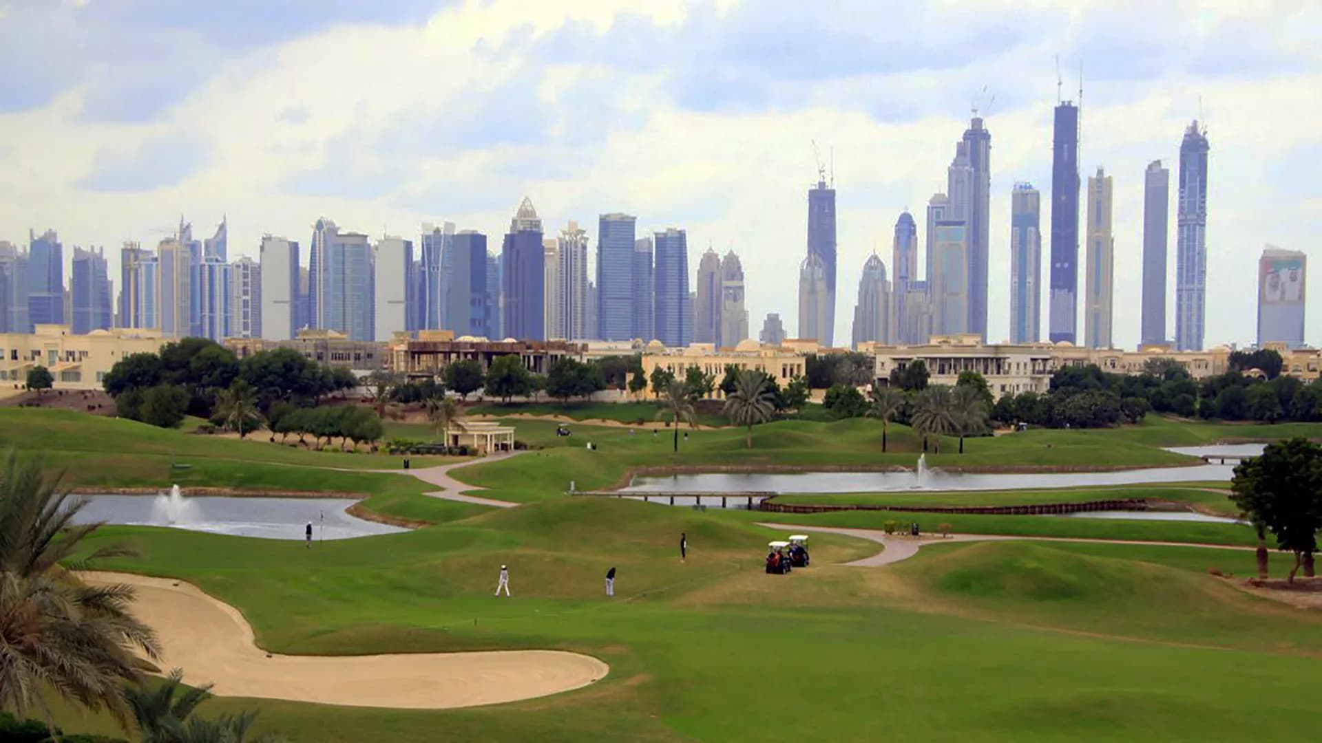 A scenic golf course with trees, water features, and a view of the towering Dubai skyline.