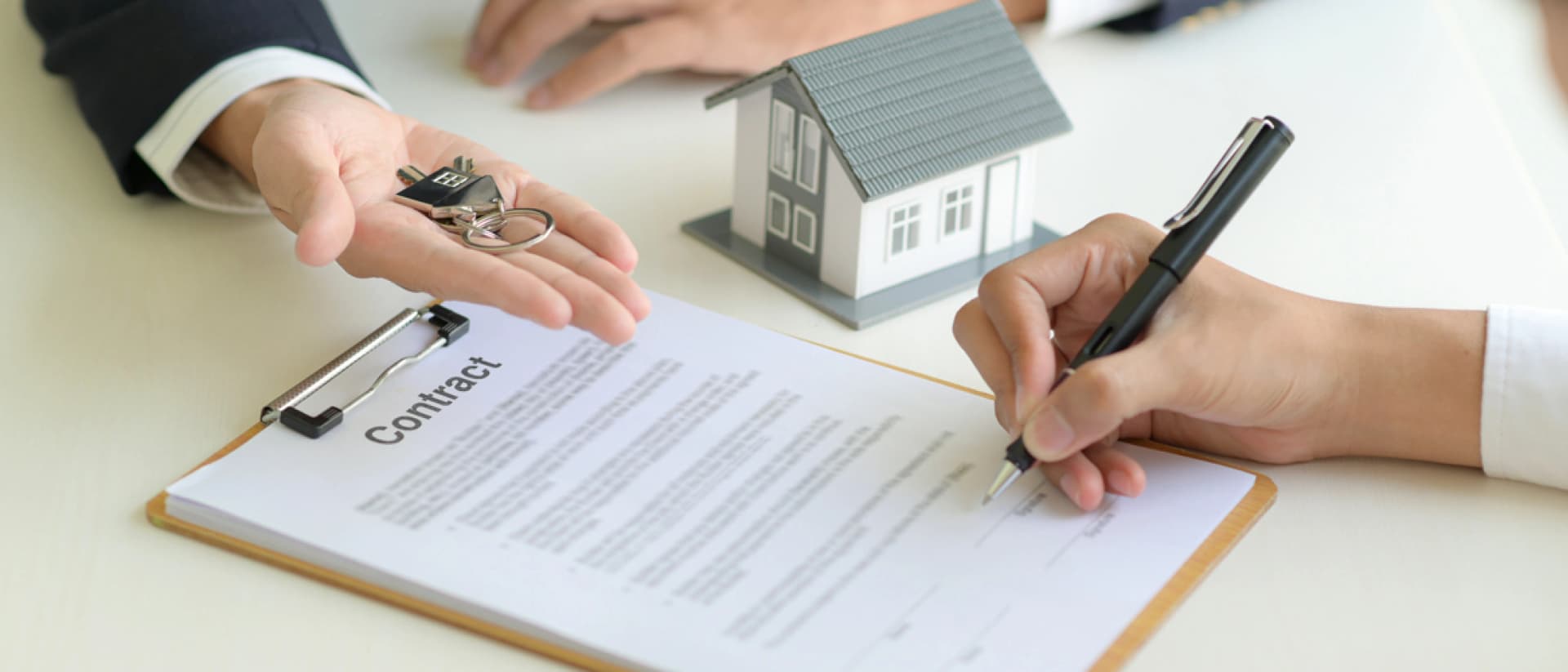 Hand signing a contract while another hand offers keys