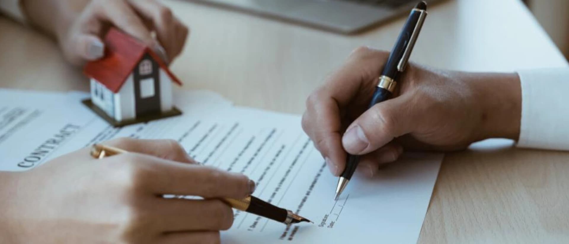 Two hands signing a contract near a small house model