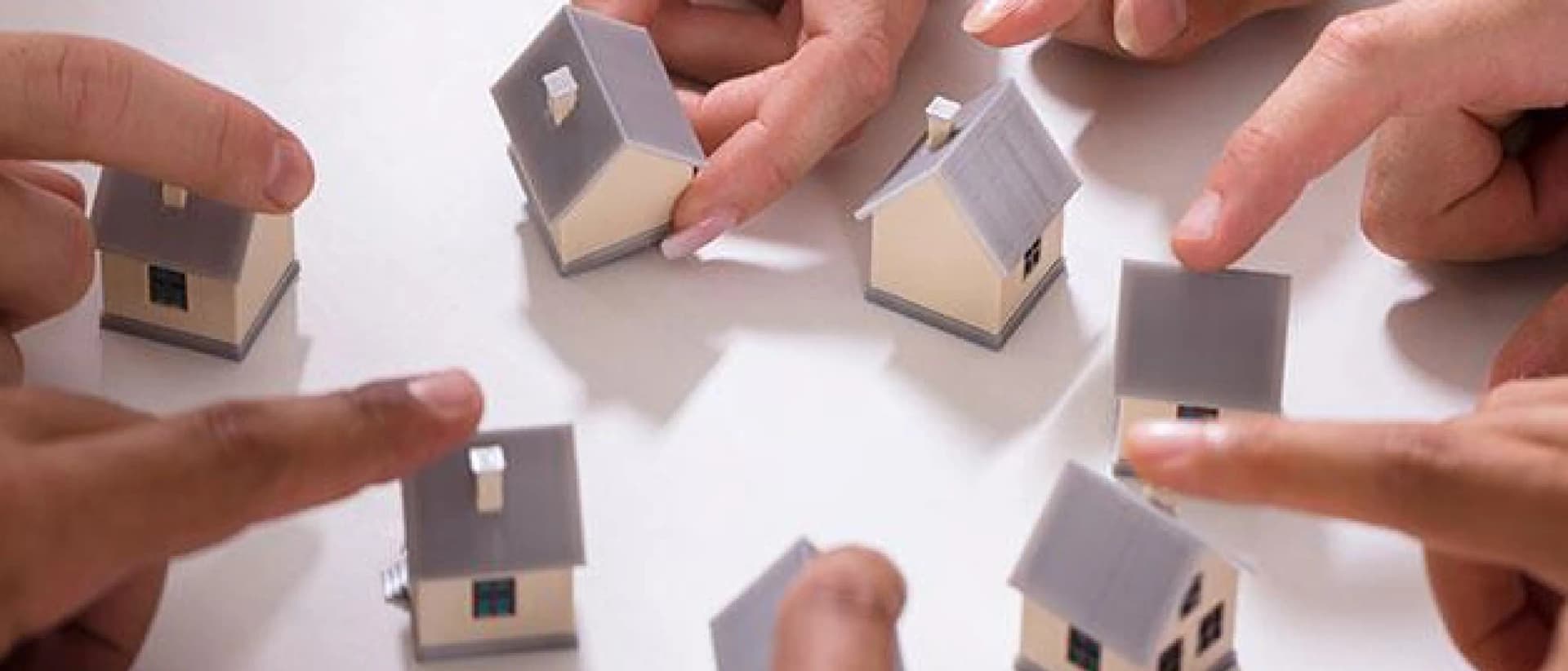 Fingers point at miniature houses on a white surface