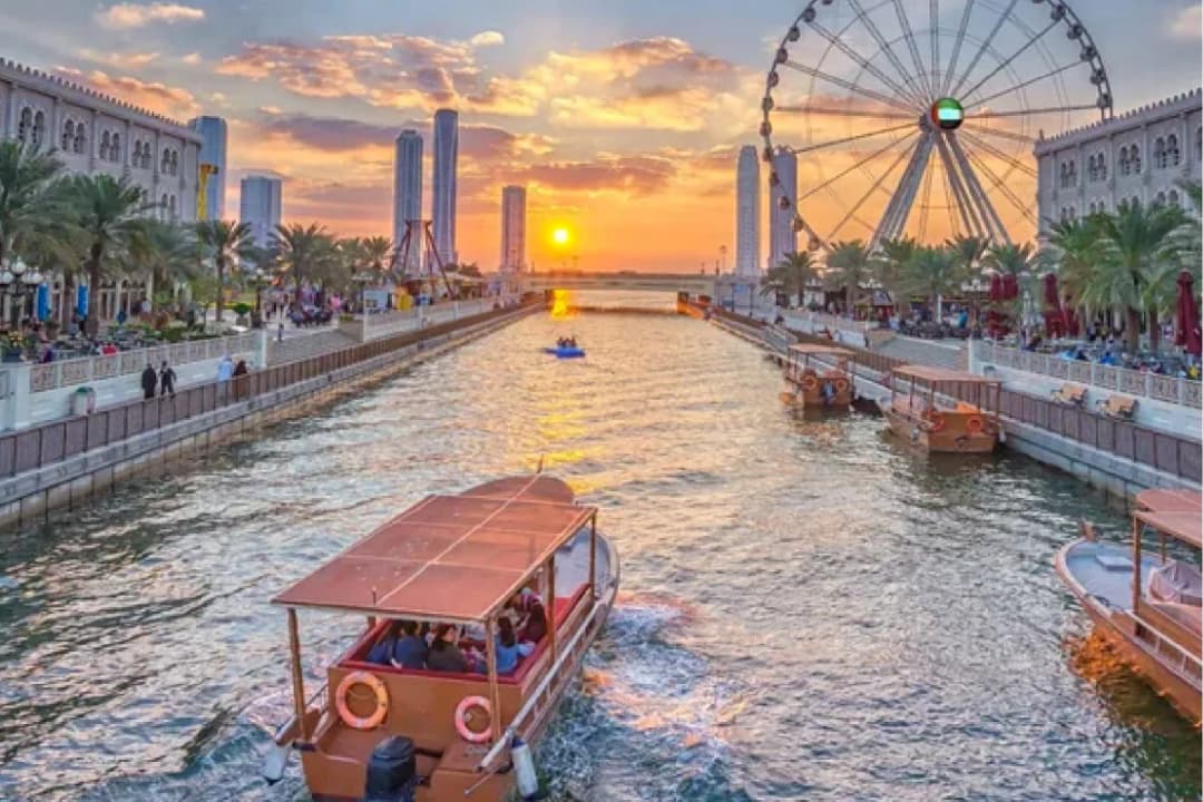 A sunset view of a canal with boats and a Ferris wheel