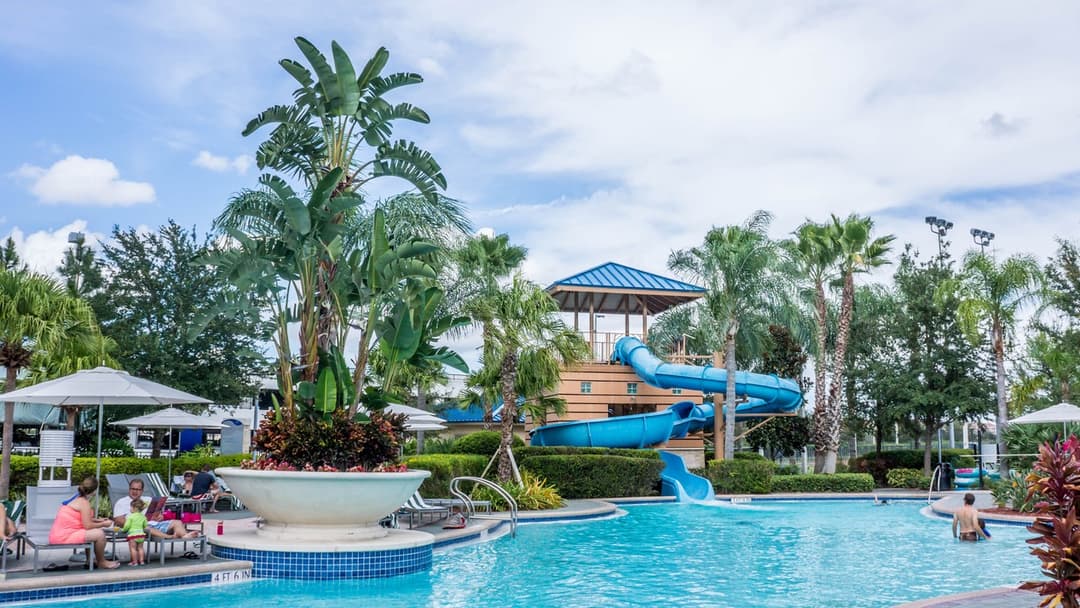 Family enjoying poolside with water slide and plants