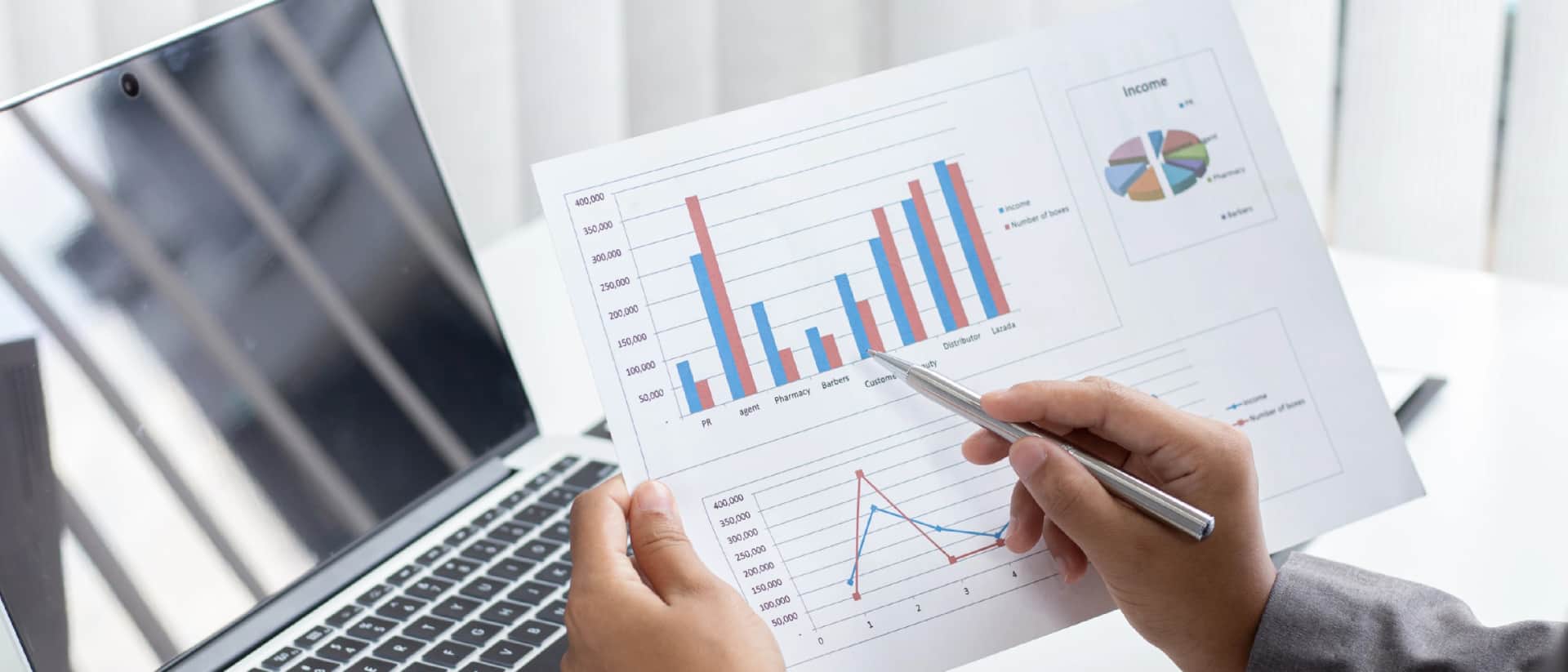 A person reviews financial documents with charts and graphs, with a laptop nearby