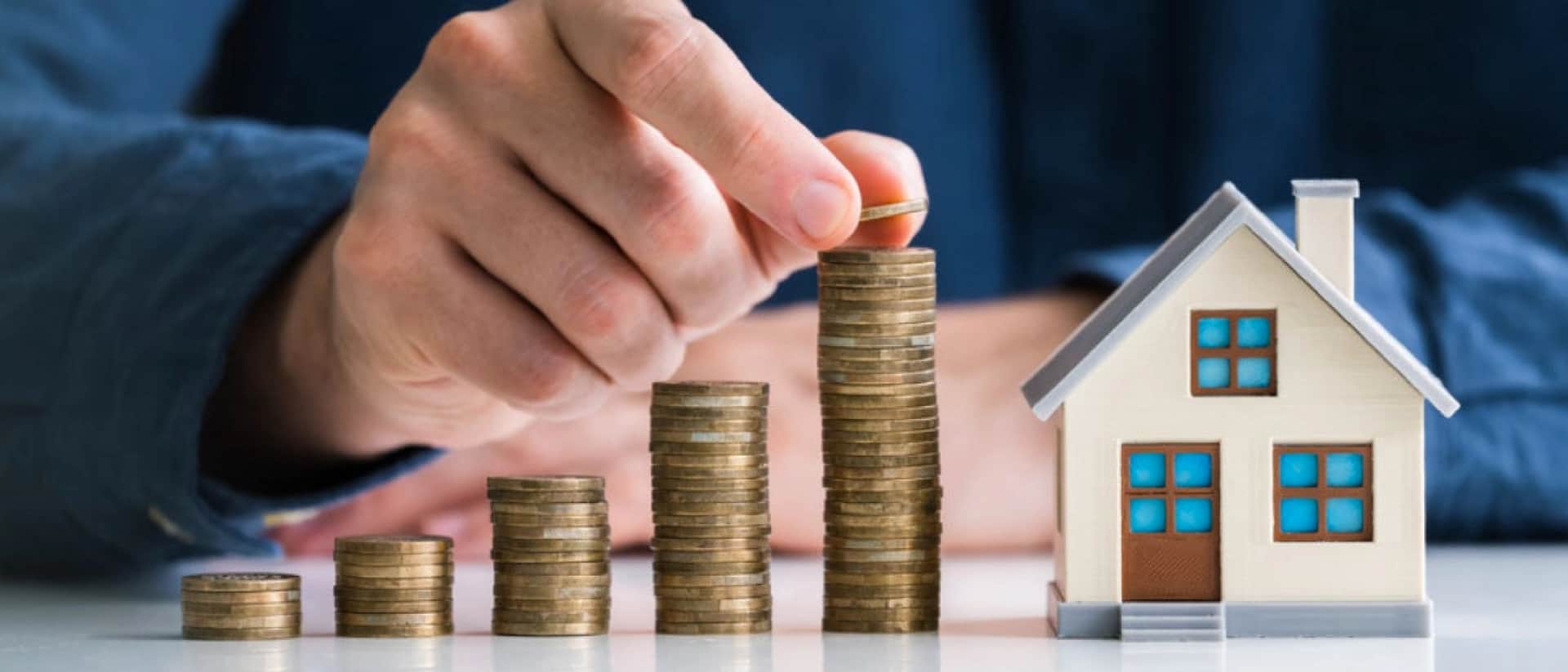 Hand stacking coins next to a small house model