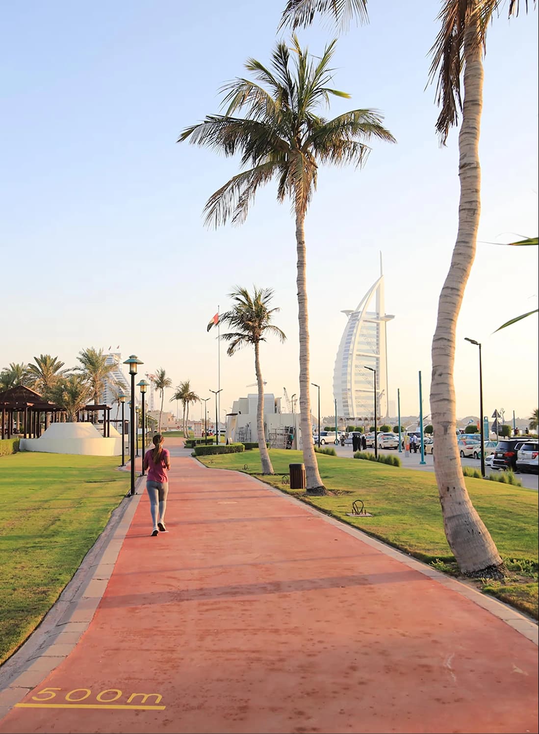 Man walking along a scenic path with palm trees and Burj Al Arab